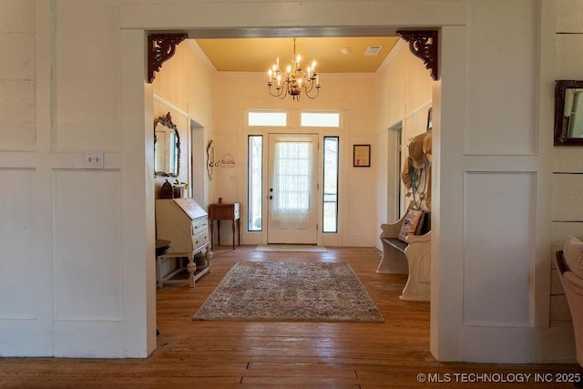 entryway with a notable chandelier, hardwood / wood-style flooring, crown molding, and visible vents