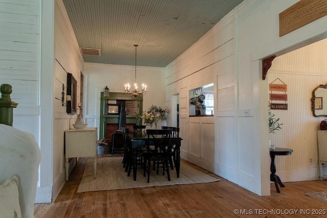 dining area with a chandelier, wooden walls, crown molding, visible vents, and hardwood / wood-style flooring