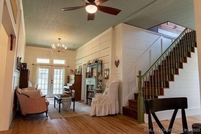 interior space featuring ceiling fan with notable chandelier, stairs, french doors, wooden walls, and wood-type flooring