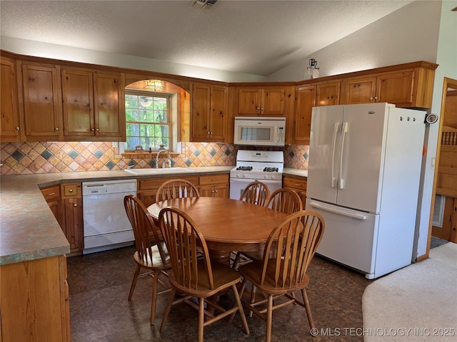 kitchen with vaulted ceiling, white appliances, brown cabinets, decorative backsplash, and a sink