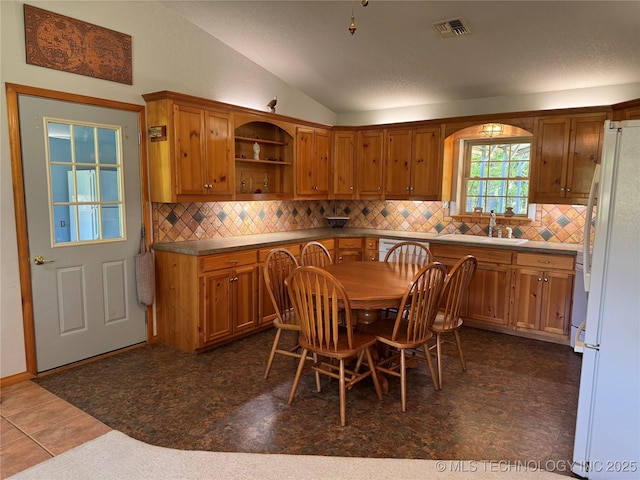 kitchen featuring freestanding refrigerator, visible vents, brown cabinets, lofted ceiling, and a sink