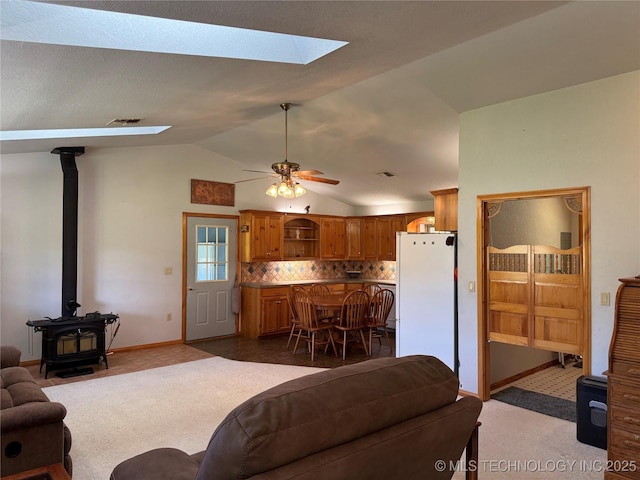 living area featuring baseboards, a ceiling fan, a wood stove, visible vents, and lofted ceiling with skylight