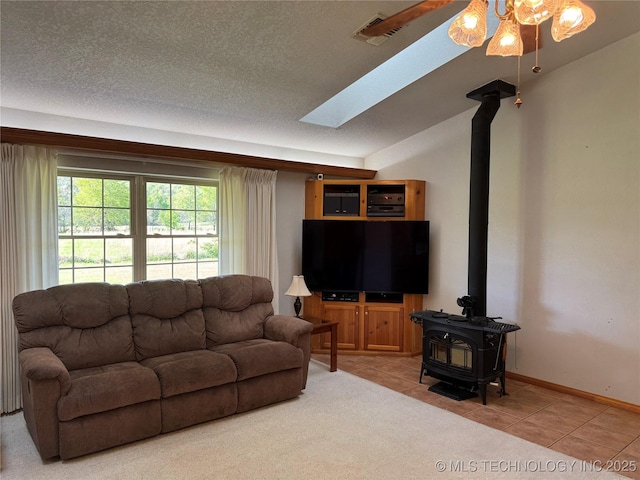 tiled living room featuring a wood stove, a textured ceiling, a ceiling fan, a skylight, and baseboards
