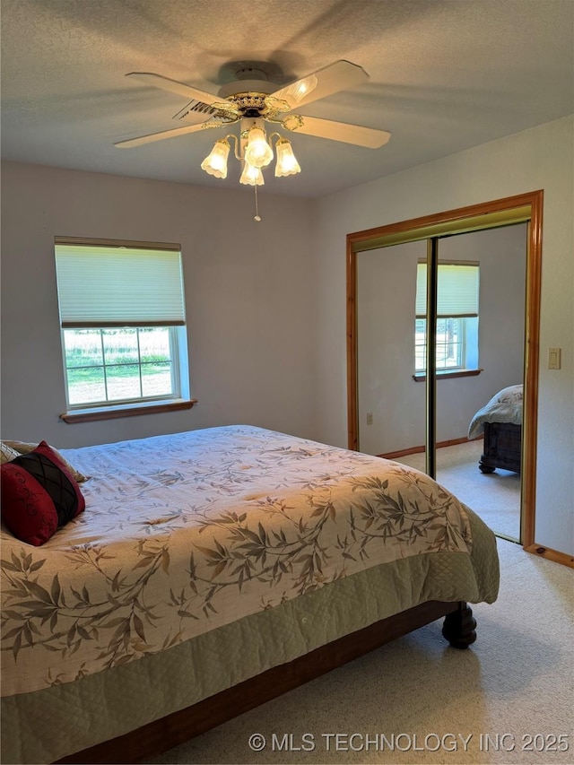 carpeted bedroom with a closet, baseboards, multiple windows, and a ceiling fan