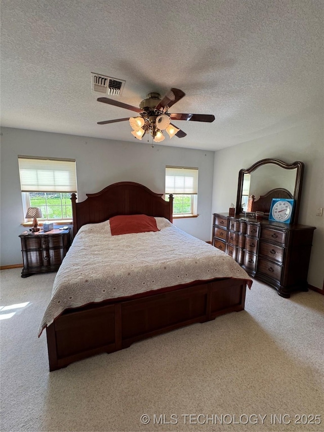 bedroom with visible vents, ceiling fan, light colored carpet, and a textured ceiling