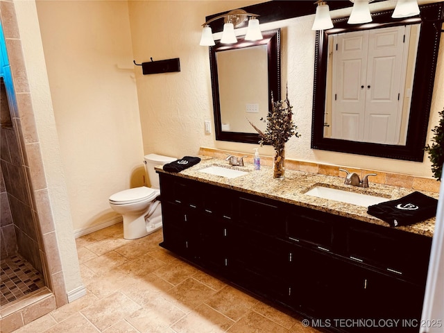 bathroom featuring toilet, double vanity, a sink, and a textured wall