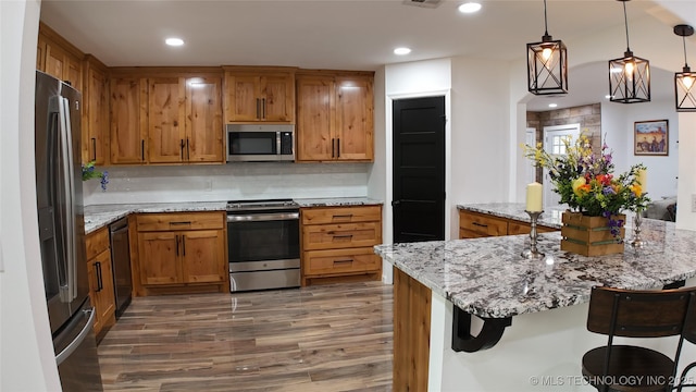 2615 E 59th St, Tulsa, OK 74105 - kitchen featuring brown cabinetry, backsplash, appliances with stainless steel finishes, wood finished floors, and a breakfast bar