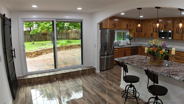 2615 E 59th St, Tulsa, OK 74105 - kitchen featuring brown cabinetry, a sink, light stone counters, a breakfast bar, and stainless steel appliances