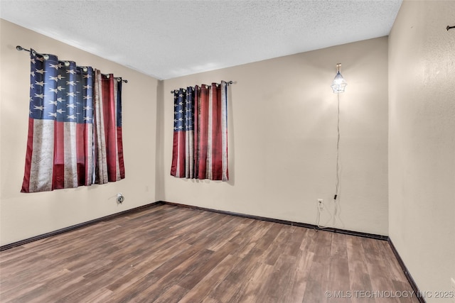 spare room with a textured ceiling, wood finished floors, and baseboards