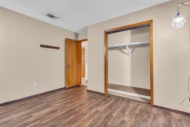 unfurnished bedroom with a textured ceiling, a closet, visible vents, wood finished floors, and baseboards