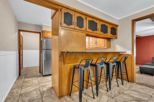 kitchen with glass insert cabinets, freestanding refrigerator, a breakfast bar, brown cabinetry, and marble finish floor