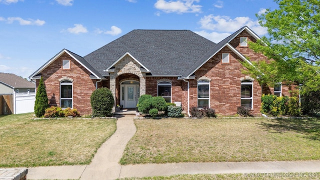 view of front facade with brick siding, a front lawn, fence, and a shingled roof