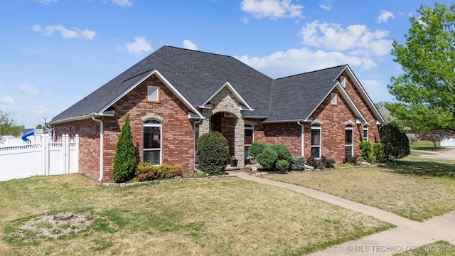view of front facade featuring a front yard, fence, brick siding, and a shingled roof