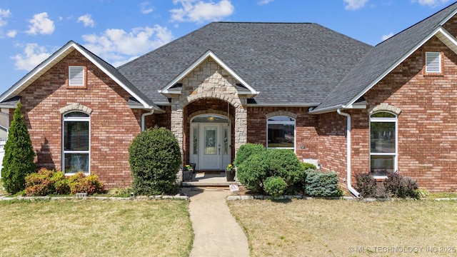 view of front facade featuring roof with shingles, a front yard, and brick siding
