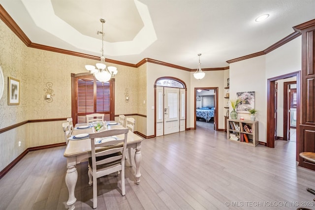 dining area featuring a raised ceiling, ornamental molding, a chandelier, wood finished floors, and a wainscoted wall