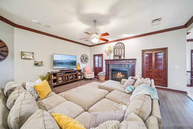 living area featuring a tiled fireplace, crown molding, visible vents, ceiling fan, and hardwood / wood-style flooring