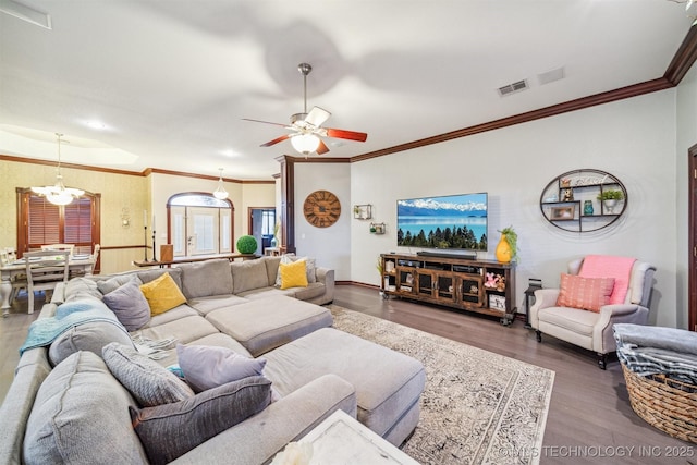 living area with baseboards, crown molding, visible vents, ceiling fan with notable chandelier, and wood finished floors