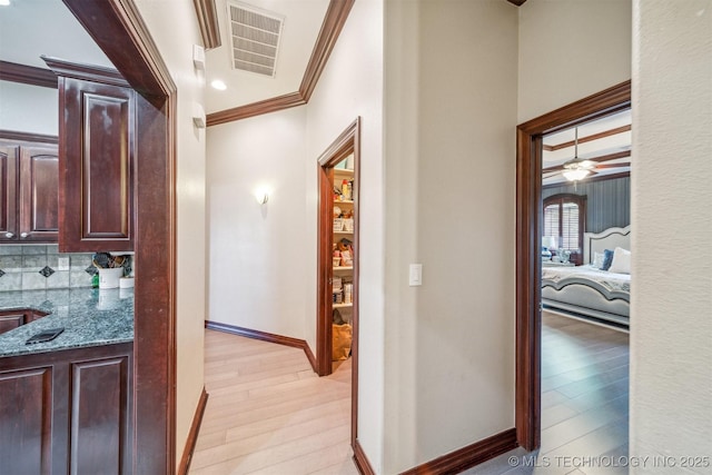 hallway featuring light wood-style floors, visible vents, baseboards, and crown molding