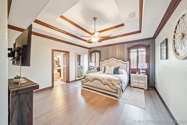 bedroom with baseboards, ensuite bathroom, crown molding, a raised ceiling, and wood finished floors