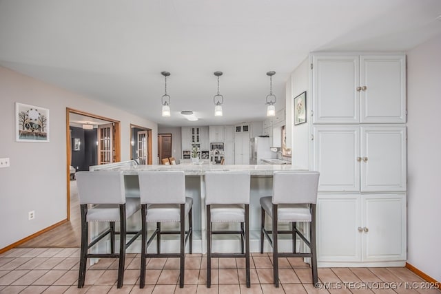 kitchen featuring white cabinets, baseboards, a peninsula, a kitchen bar, and pendant lighting