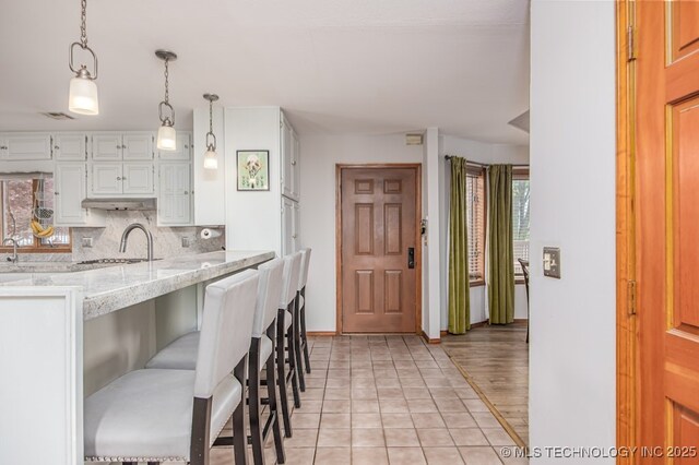 kitchen featuring white cabinetry, a breakfast bar, light stone counters, backsplash, and plenty of natural light