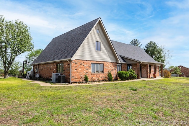 view of home's exterior with a yard, a shingled roof, central AC unit, and brick siding