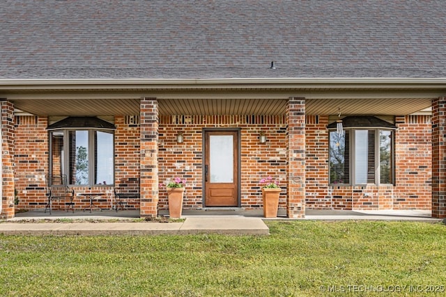 doorway to property with roof with shingles, a yard, and brick siding