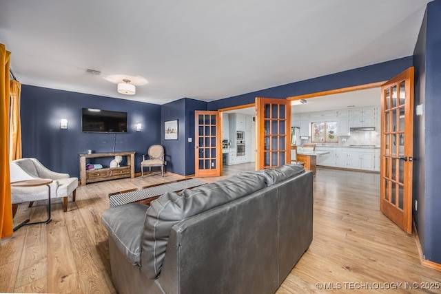 living room with light wood-type flooring, french doors, and visible vents