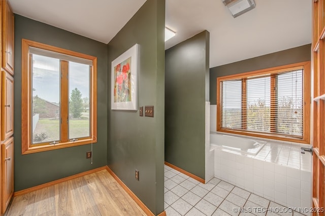 interior space featuring a bath, baseboards, and a healthy amount of sunlight