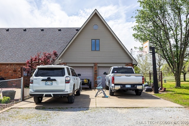 view of side of home with a shingled roof, concrete driveway, fence, and brick siding