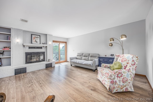 living area with visible vents, a brick fireplace, wood finished floors, and built in features