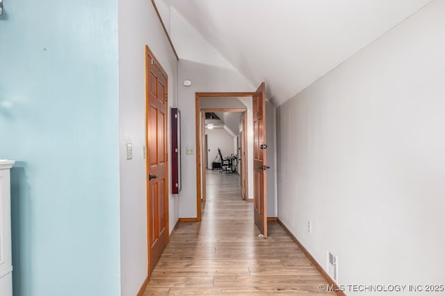 hall with baseboards, light wood finished floors, and vaulted ceiling