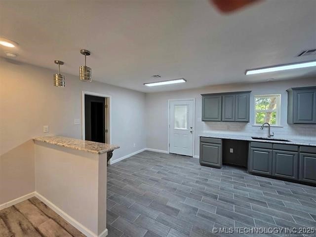 kitchen with tasteful backsplash, visible vents, a sink, hanging light fixtures, and baseboards