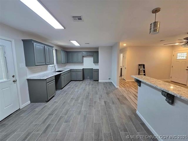 kitchen with gray cabinetry, light wood-style flooring, visible vents, a sink, and baseboards