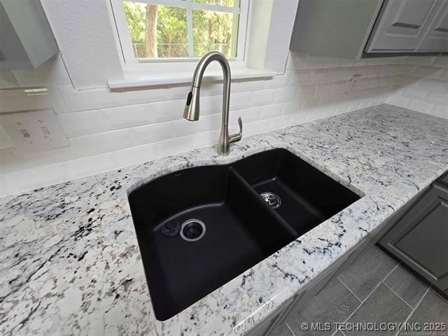 interior details with gray cabinets, a sink, backsplash, and light stone counters