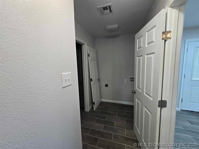 hall featuring wood finish floors, baseboards, a textured wall, and visible vents