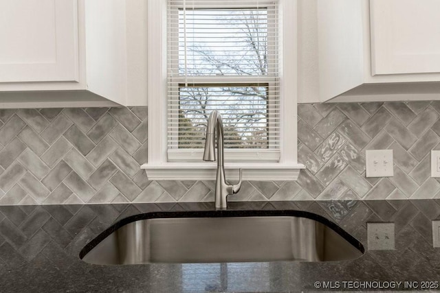 interior details with decorative backsplash, a sink, and white cabinetry