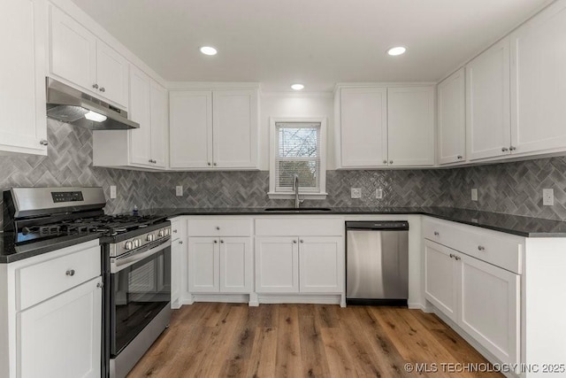 kitchen featuring a sink, dark countertops, under cabinet range hood, white cabinetry, and stainless steel appliances