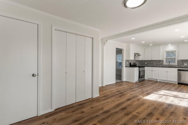 kitchen with appliances with stainless steel finishes, decorative backsplash, dark countertops, and wood finished floors