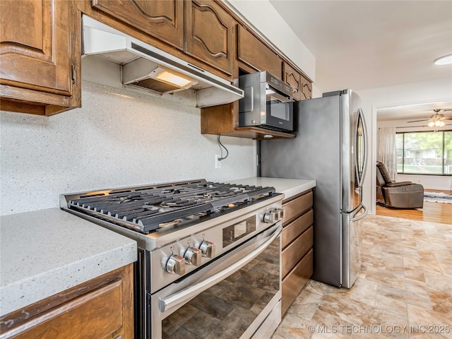 kitchen with under cabinet range hood, brown cabinets, ceiling fan, and appliances with stainless steel finishes