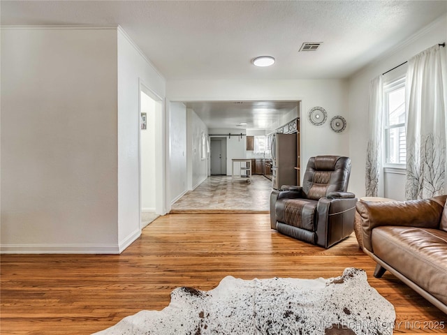 living room with baseboards, ornamental molding, light wood-type flooring, and visible vents