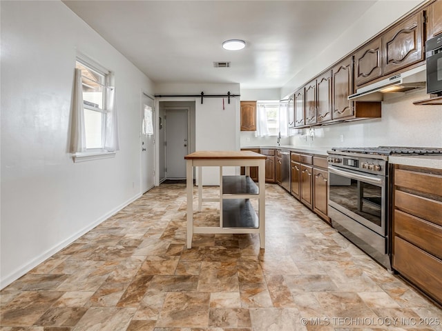 kitchen with a barn door, stainless steel appliances, a healthy amount of sunlight, under cabinet range hood, and visible vents