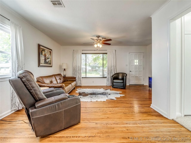 living area with visible vents, ornamental molding, baseboards, a ceiling fan, and light wood finished floors