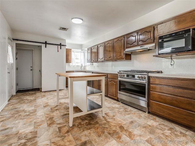 338 E 45th Pl, Tulsa, OK 74105 - kitchen featuring gas range, under cabinet range hood, black microwave, a barn door, and stone finish floors
