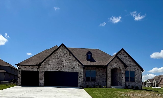 french country home featuring brick siding, driveway, roof with shingles, a front yard, and an attached garage