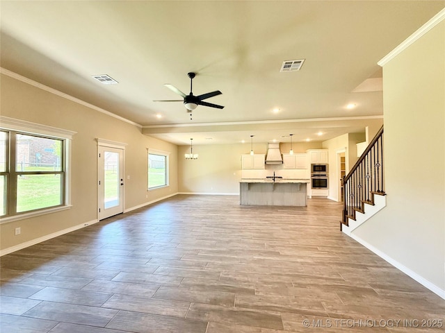 unfurnished living room with ornamental molding, visible vents, ceiling fan, and baseboards