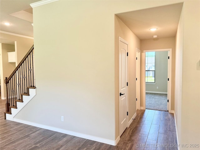 corridor featuring crown molding, baseboards, stairway, and dark wood-type flooring