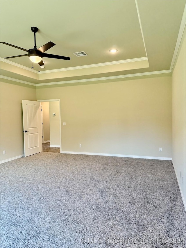 empty room with crown molding, visible vents, ceiling fan, and a raised ceiling