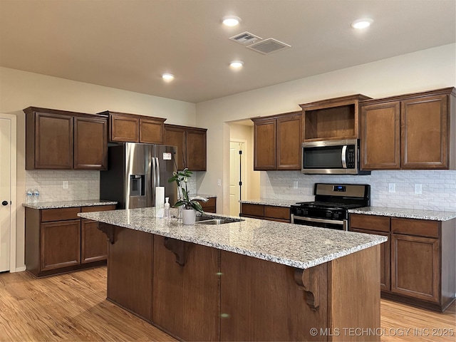 6370 E 124th Ct, Bixby, OK 74008 - kitchen featuring appliances with stainless steel finishes, light wood finished floors, a breakfast bar, tasteful backsplash, and a kitchen island with sink