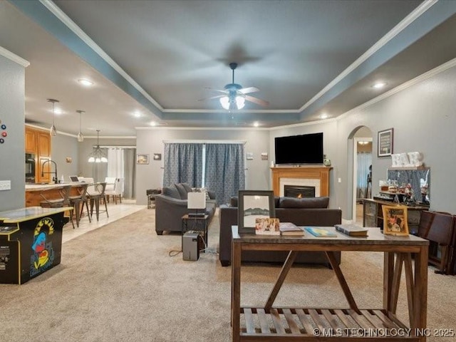 living room with a tray ceiling, light carpet, ceiling fan, and ornamental molding
